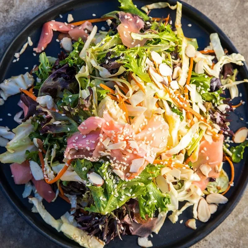 Fresh salad with mixed greens, carrots, pale pink slices, sesame, almonds.