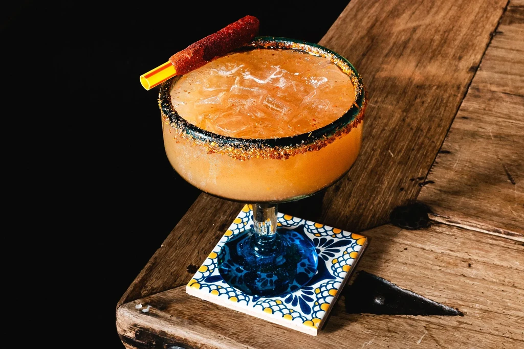 Amber cocktail with chili-spiced rim, candy stick, and Talavera coaster.
