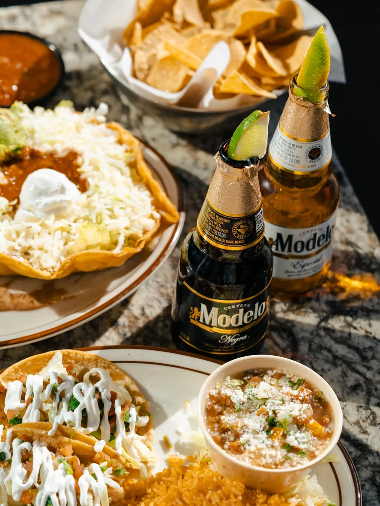 Tabletop with tacos, rice, stew, beer bottles, chips, and salsa.