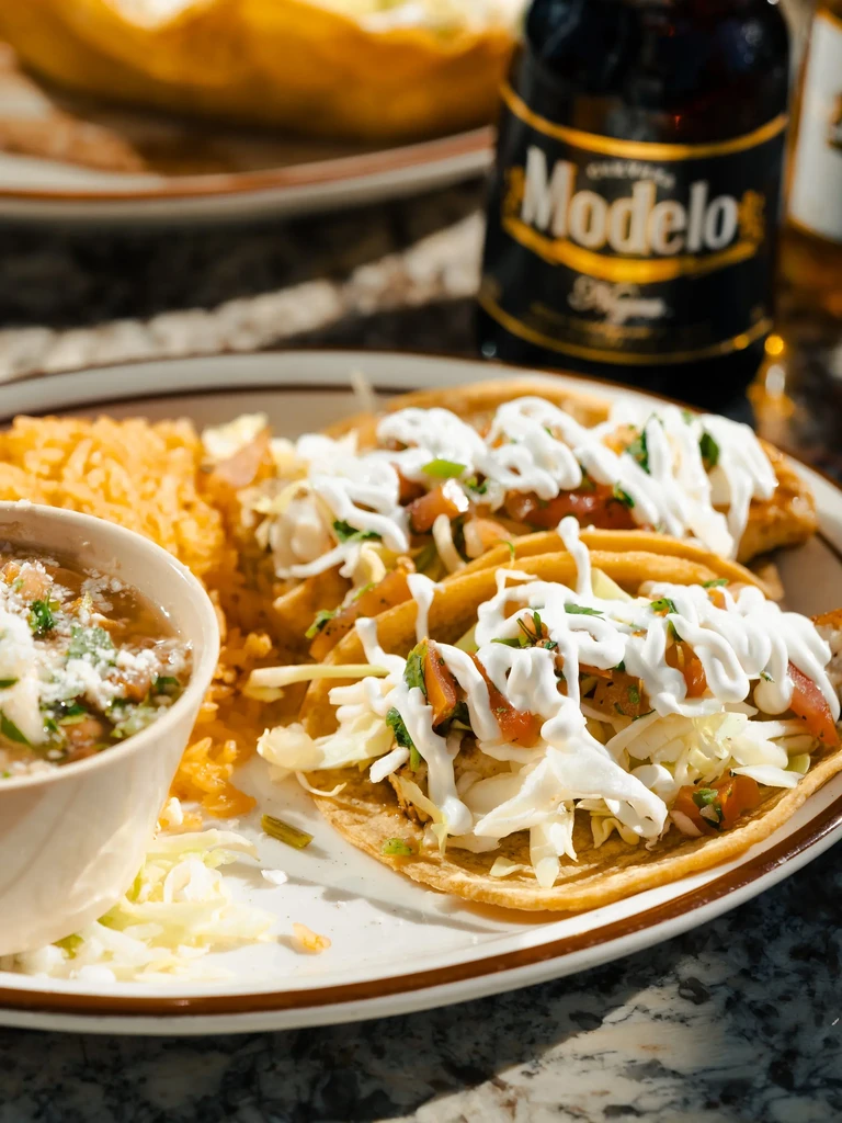 Plate of two Mexican tacos, rice, beans, and Modelo beer.