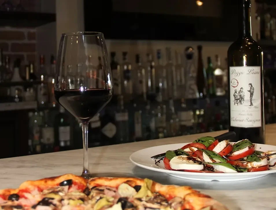 Pizza, caprese salad, and red wine on a bar counter.