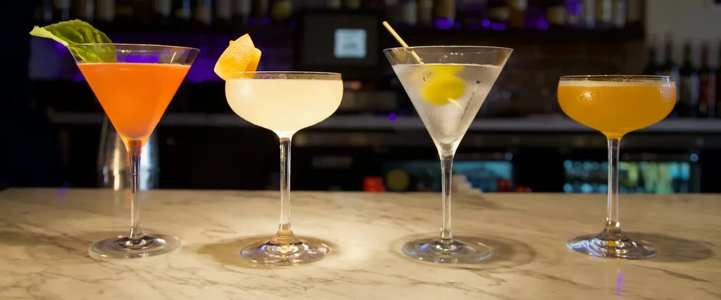 Four distinct cocktails lined up on a marble bar counter.