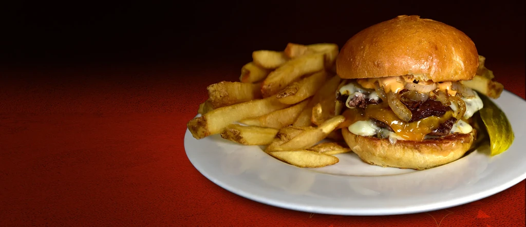 Stacked burger, golden fries, and pickle on a white plate.