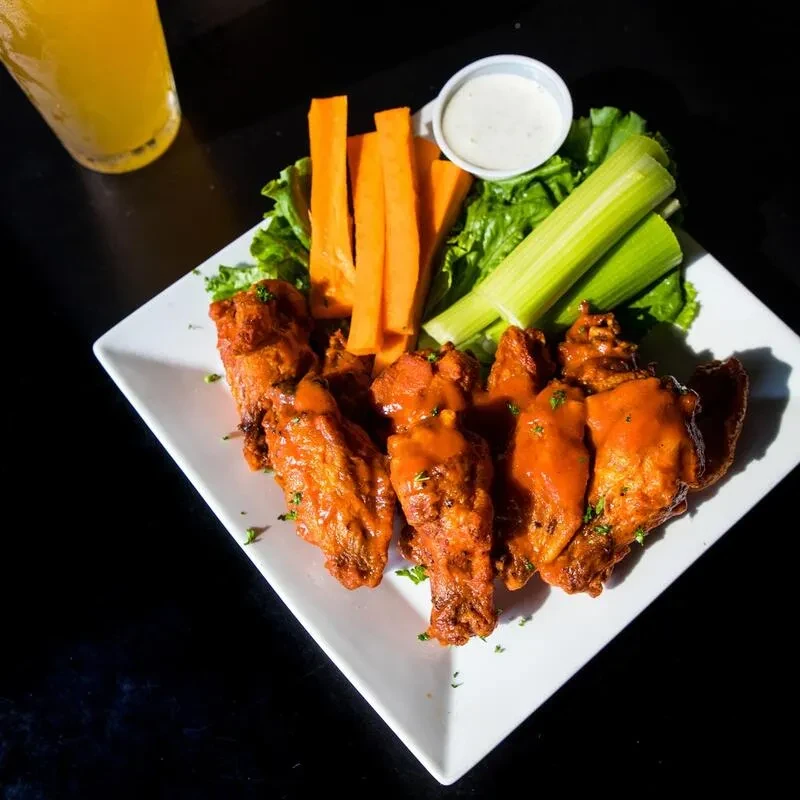 Plate of buffalo chicken wings with carrots, celery, and dipping sauce.