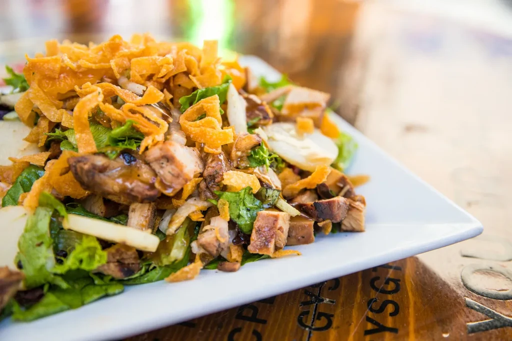 Close-up of a chicken salad with greens, grilled chicken, and crispy wontons.