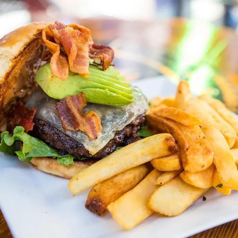 Gourmet burger with cheese, bacon, avocado, lettuce, and golden wedge fries.