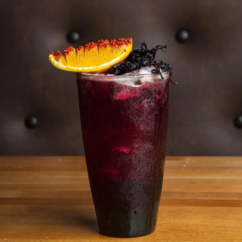 Reddish-purple iced drink with spiced orange slice and dried flowers.