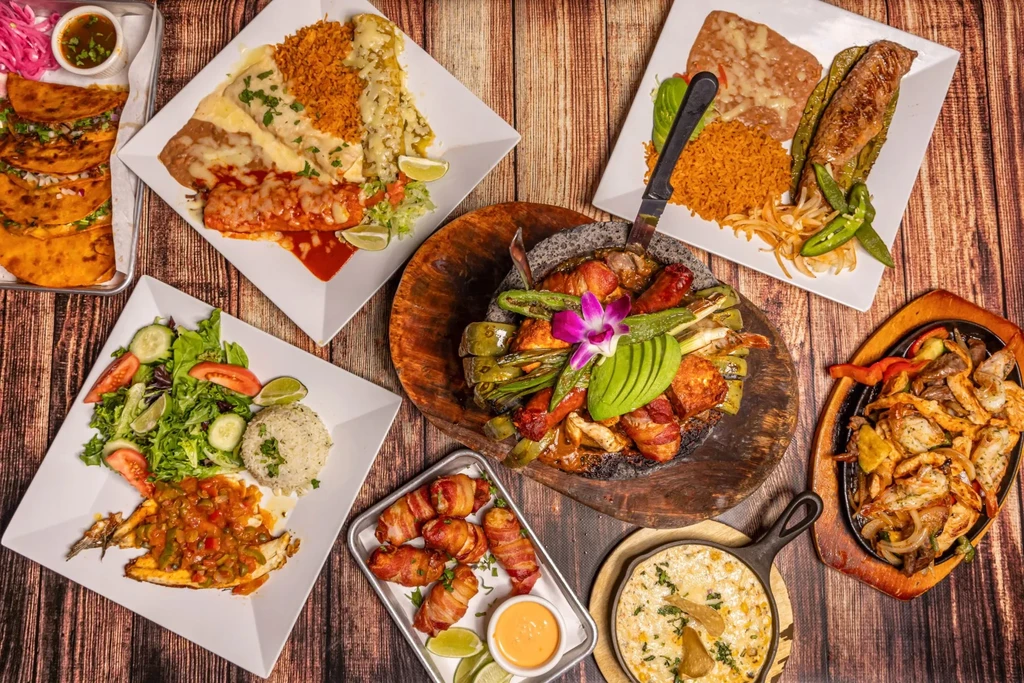 Flat-lay of diverse Mexican and Tex-Mex dishes on wood.