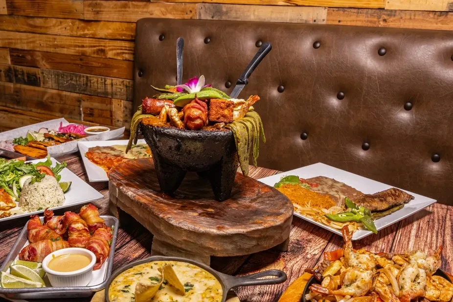 Large molcajete filled with meats, avocado, and chiles on a table.