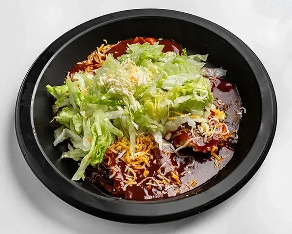 Black bowl of dark stew topped with shredded lettuce and cheese.