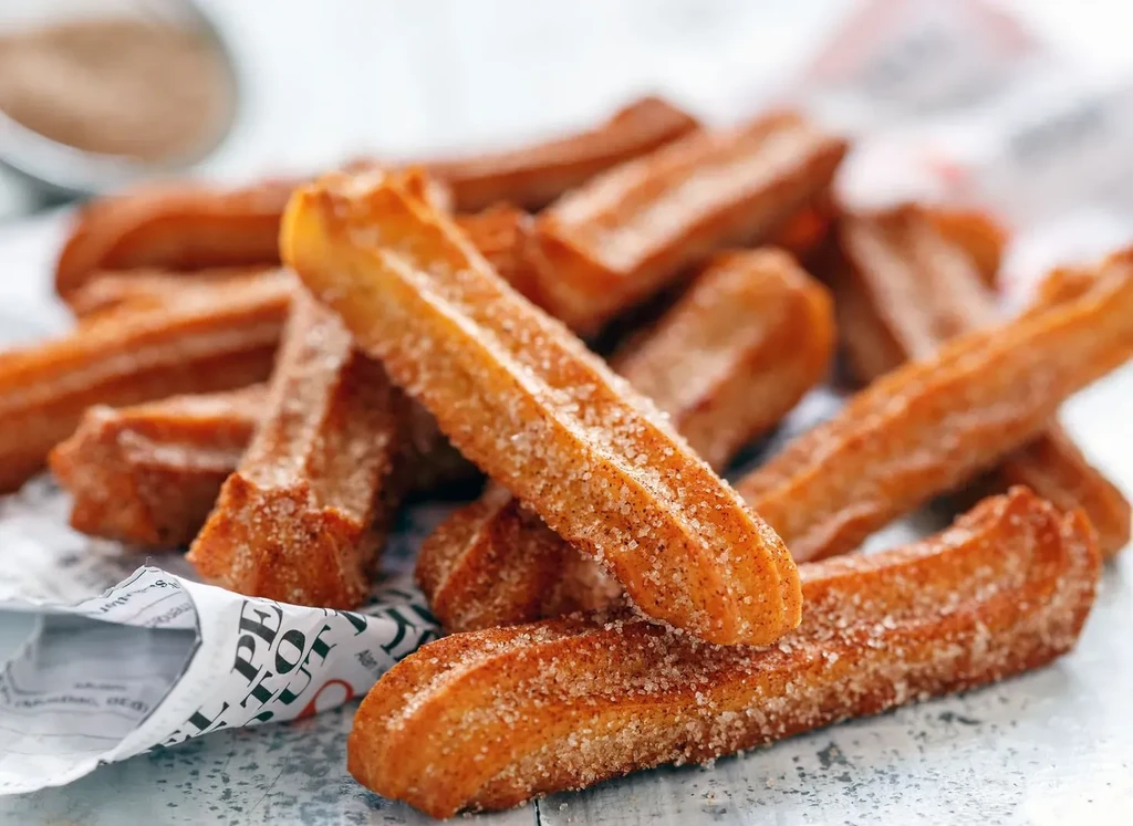 Golden-brown ridged churros piled high, coated with sugar and cinnamon.
