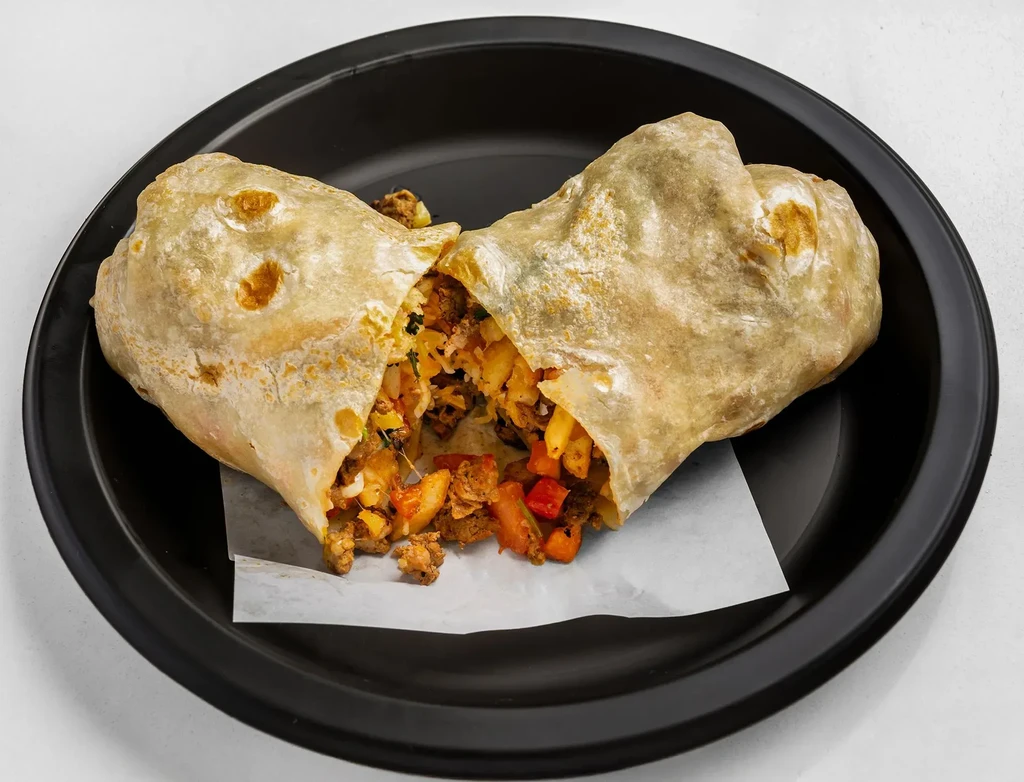 Halved burrito reveals meat, rice, potato, and vegetable filling on a plate.