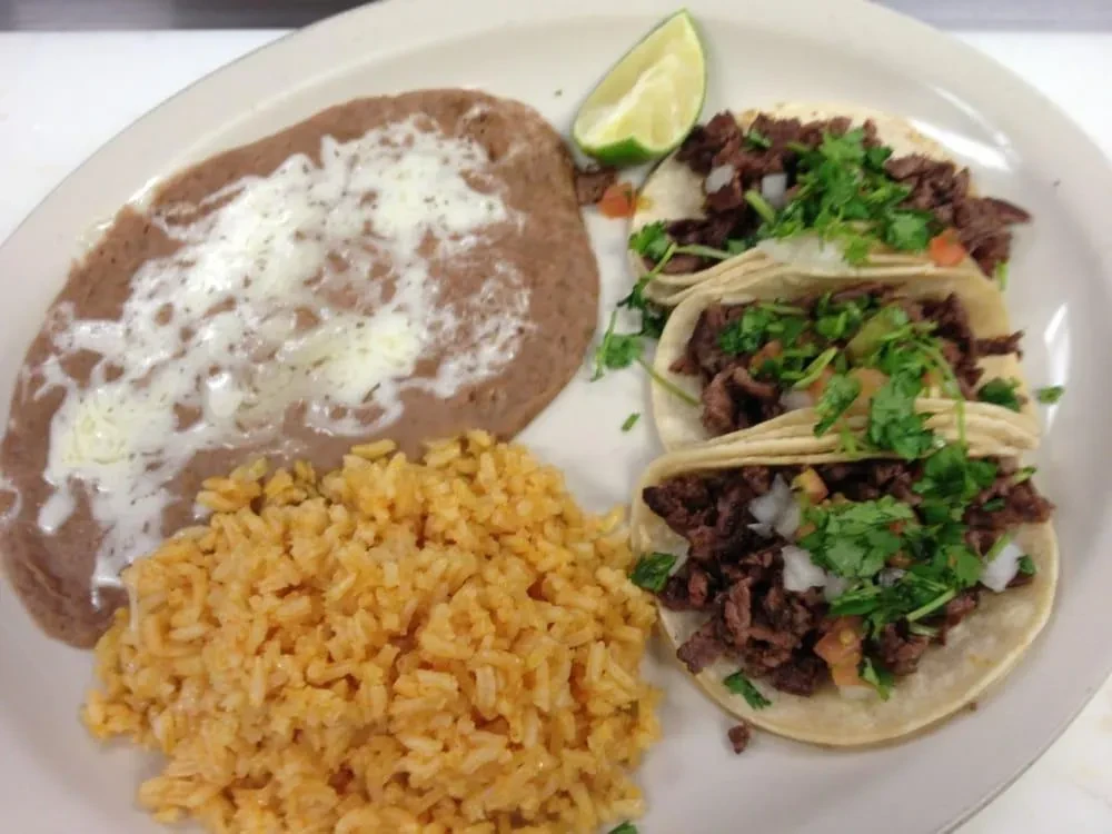 Plate of three street-style tacos, refried beans, and Spanish rice.