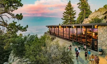 Modern building with glass and stone reflects colorful mountain sunset.