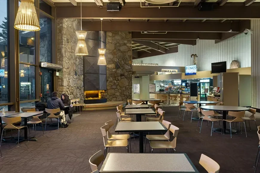 Lodge restaurant interior with a stone fireplace, tables, and Peaks Restaurant sign.