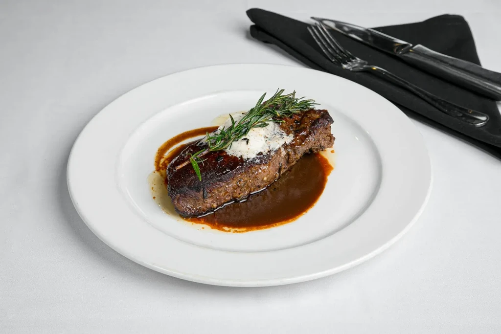 Professionally plated seared steak with gravy, white topping, and rosemary.