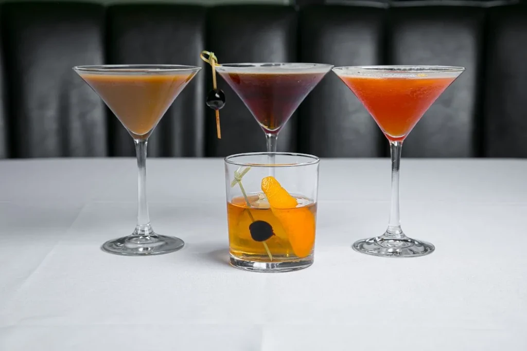 Four colorful, garnished cocktails in glasses on a white tablecloth.