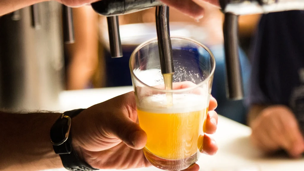 Hand pouring frothy golden beer from a tap into a clear glass.