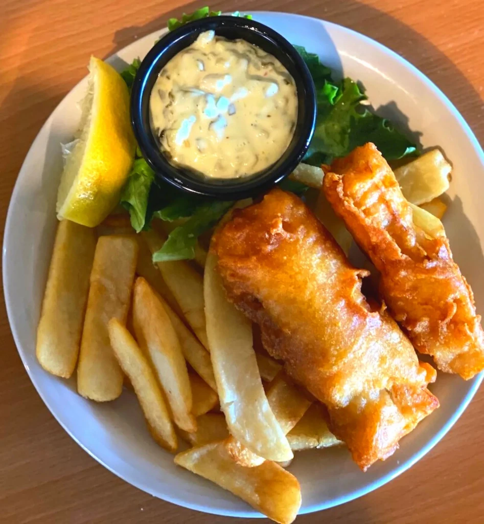Plate of golden fish and chips with tartar sauce, lemon, and lettuce.