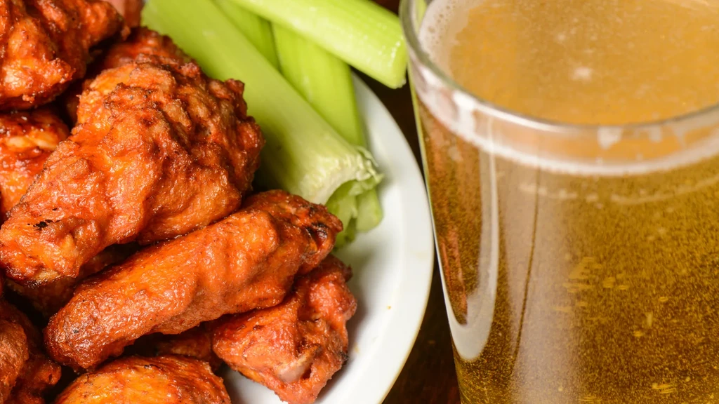 Plate of buffalo chicken wings, celery sticks, and a glass of beer.