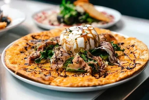 Flatbread pizza with burrata, cured meat, arugula, and balsamic glaze.