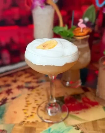 Frothy cocktail in a coupe glass, garnished with a banana slice.
