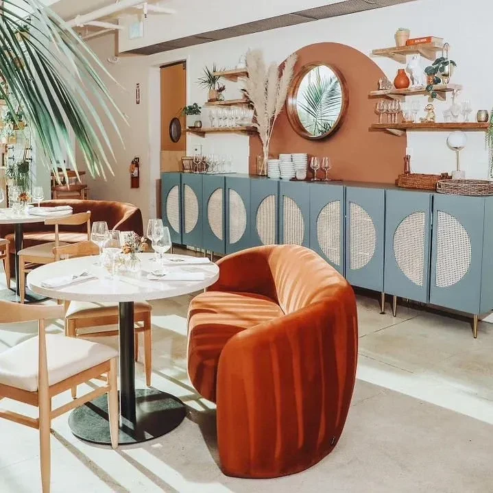 Modern restaurant dining space with velvet chair and terracotta arch mirror.