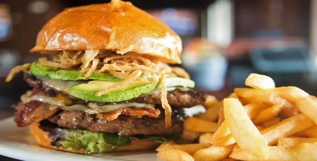 Gourmet burger with brioche bun, bacon, avocado, onion strings, and fries.