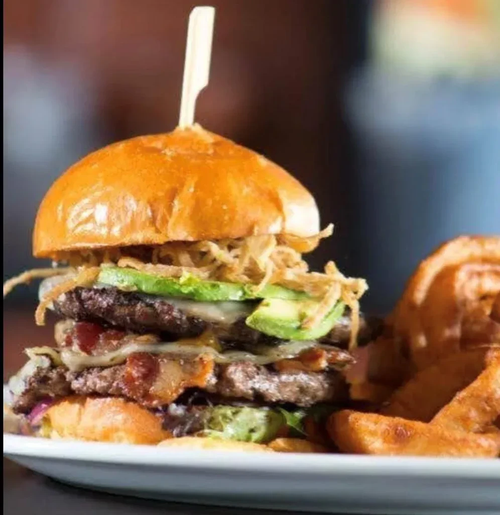 Multi-layered burger with beef, bacon, avocado, cheese, and fried onions.
