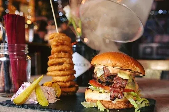 Gourmet burger, tall onion rings, and sides with dramatic smoke presentation.