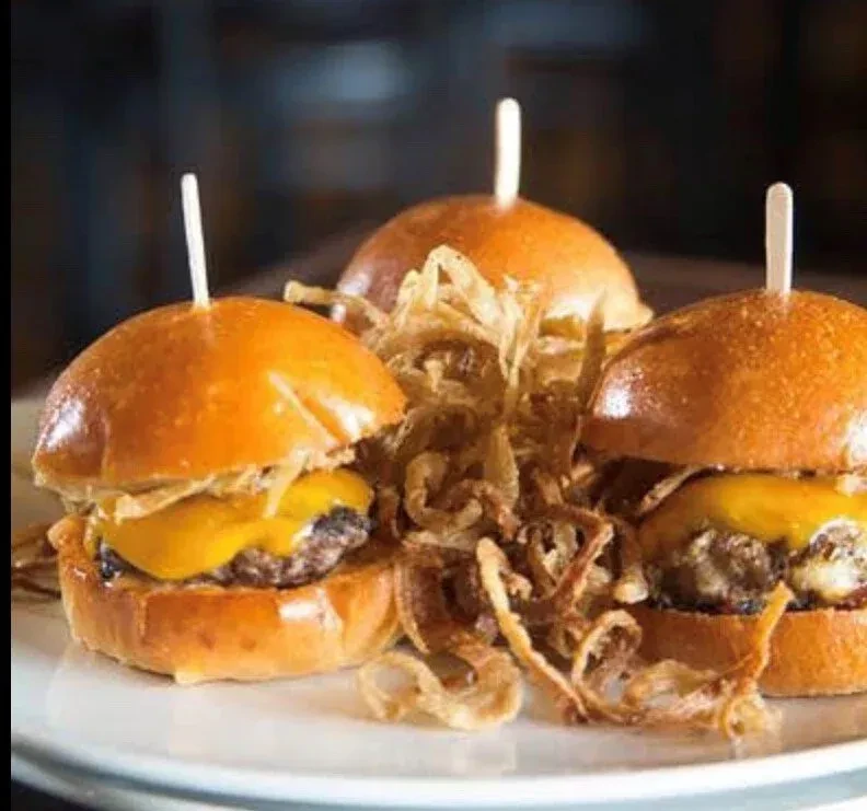 Three brioche cheeseburger sliders with melted cheese and crispy fried onions.