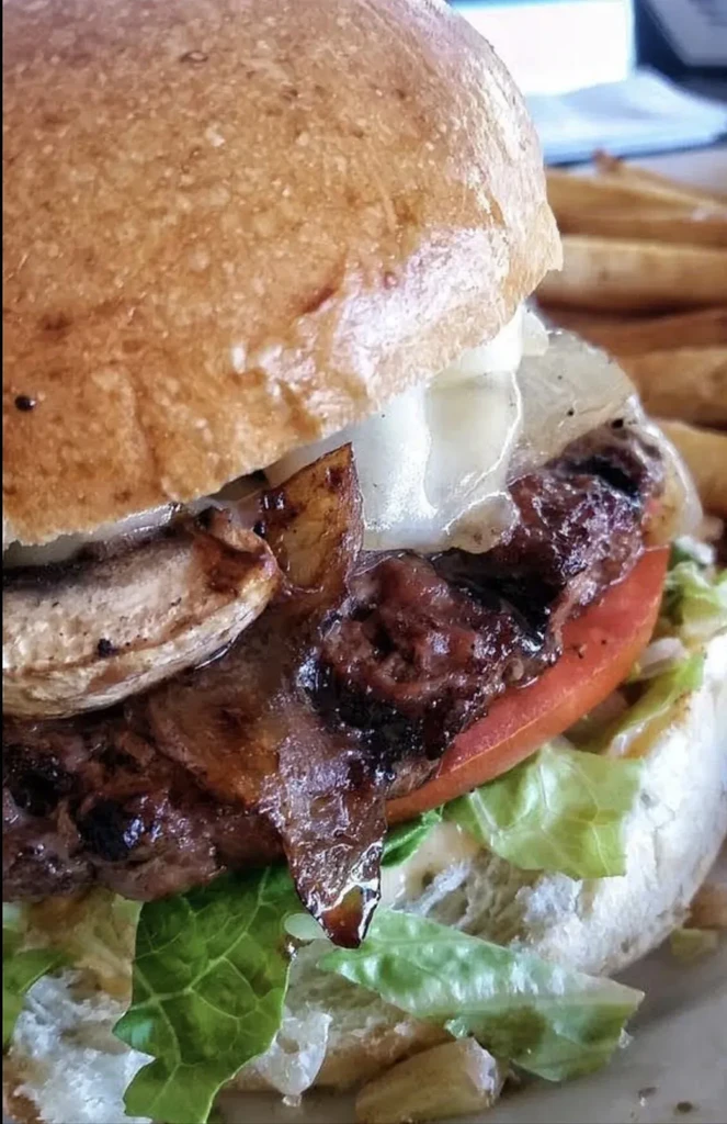 Gourmet burger with bun, melted cheese, beef patty, and fresh vegetables.