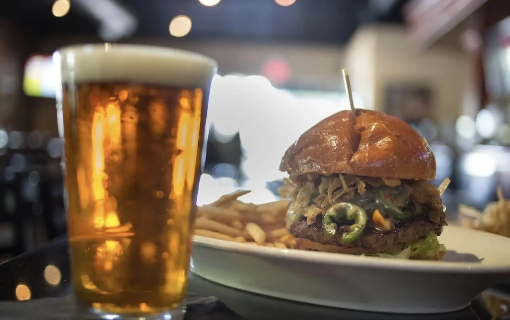 Close-up of gourmet burger with skewer, fries, and amber beer.