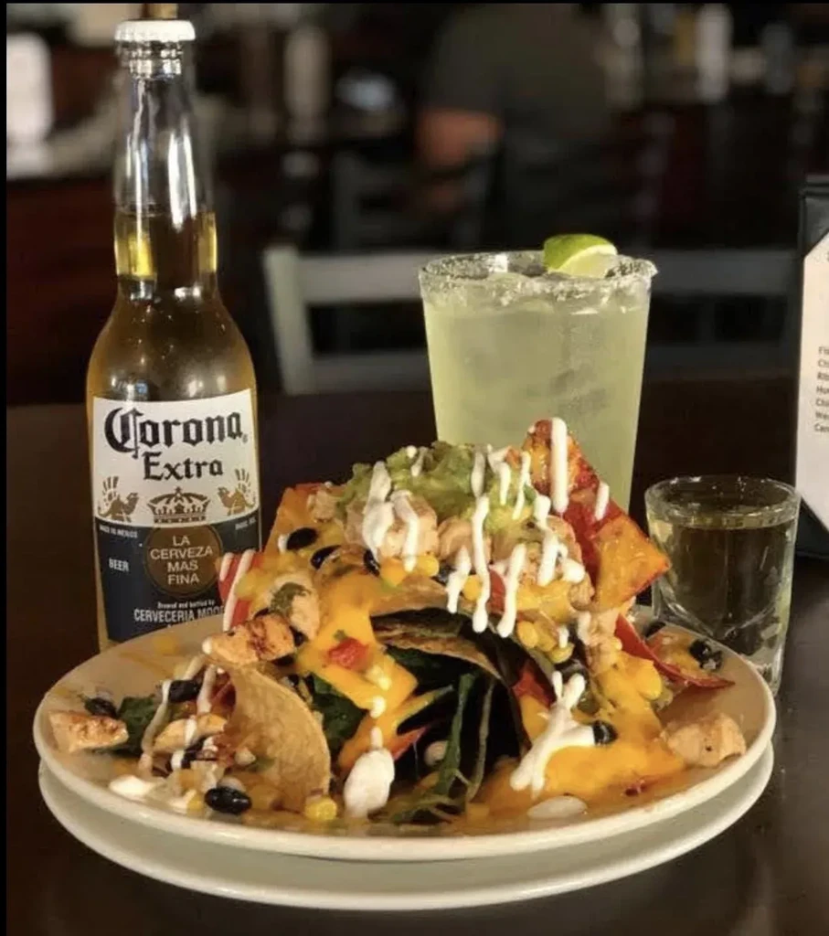 Loaded nachos, Corona beer, margarita, and a shot on a restaurant table.