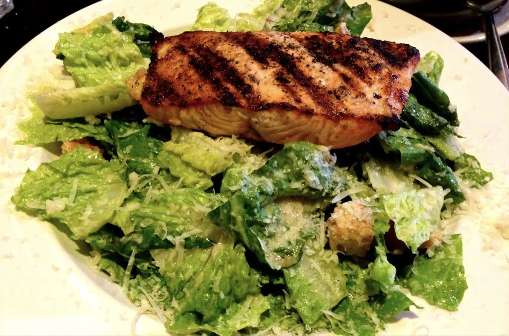 Close-up of grilled salmon on Caesar salad with Parmesan.