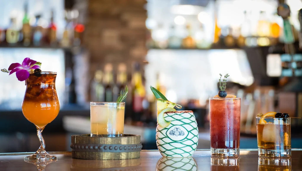 Five distinct, garnished cocktails on a glossy bar counter.