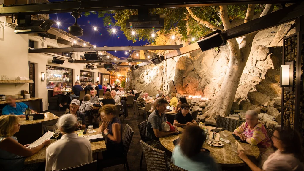 Lively restaurant patio at night with string lights and a rock wall fire pit.