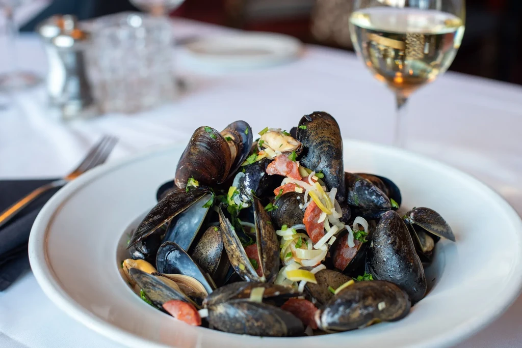 Mussels in a white bowl, garnished with herbs and red pepper.