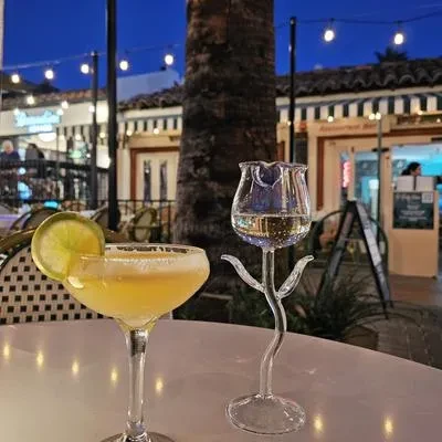 Yellow and clear cocktails on a table at an illuminated outdoor bar.