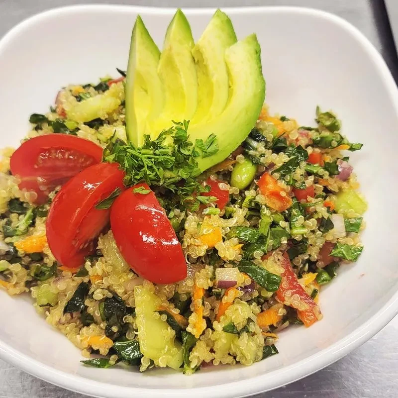 Vibrant quinoa salad with mixed vegetables, avocado, tomatoes, and herbs.