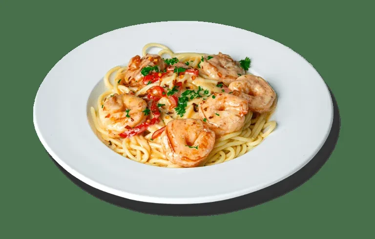 Creamy shrimp pasta garnished with green herbs and red flakes.