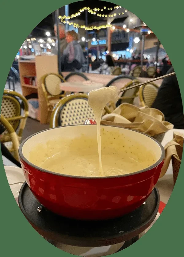 Fork lifts food from bubbling cheese fondue, dripping into red pot.