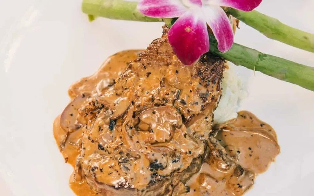 Meat with brown sauce, mushrooms, asparagus, and a purple orchid.