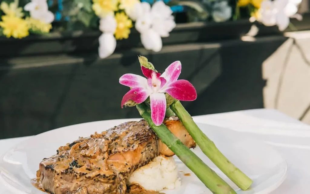 Plated main course: seared protein, creamy sauce, mashed potatoes, asparagus, orchid.