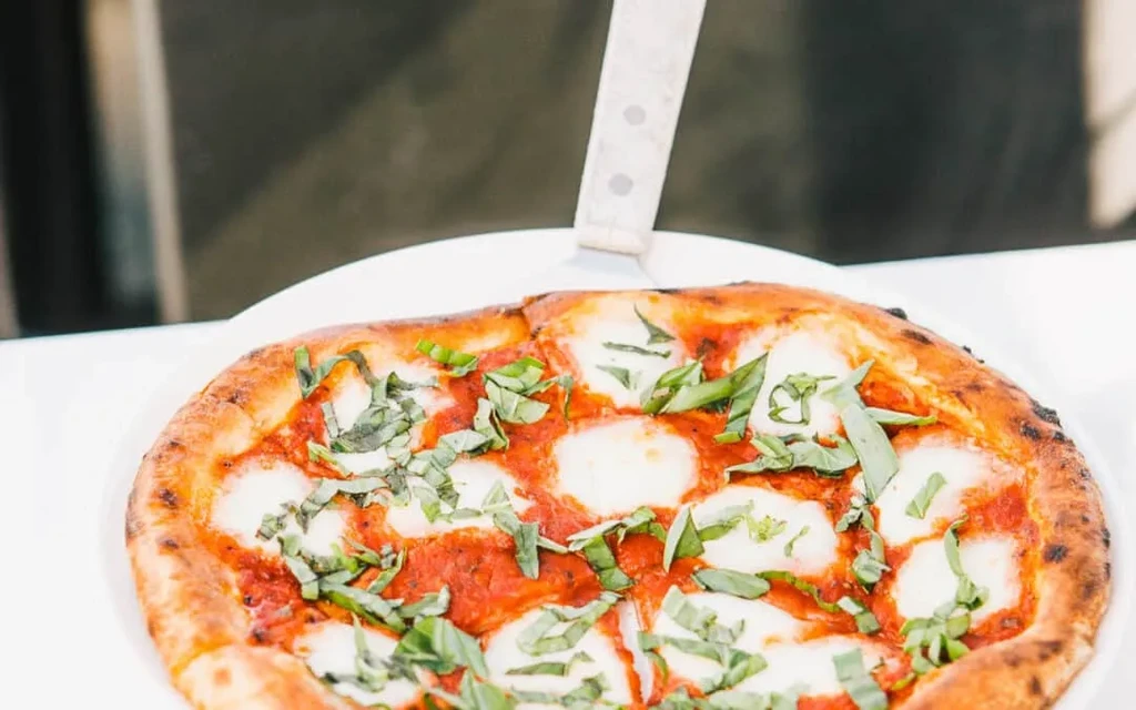 Close-up of sliced Margherita pizza with basil, mozzarella, and crispy crust.