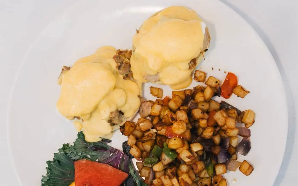 Breakfast plate with creamy Eggs Benedict, home fries, and watermelon.