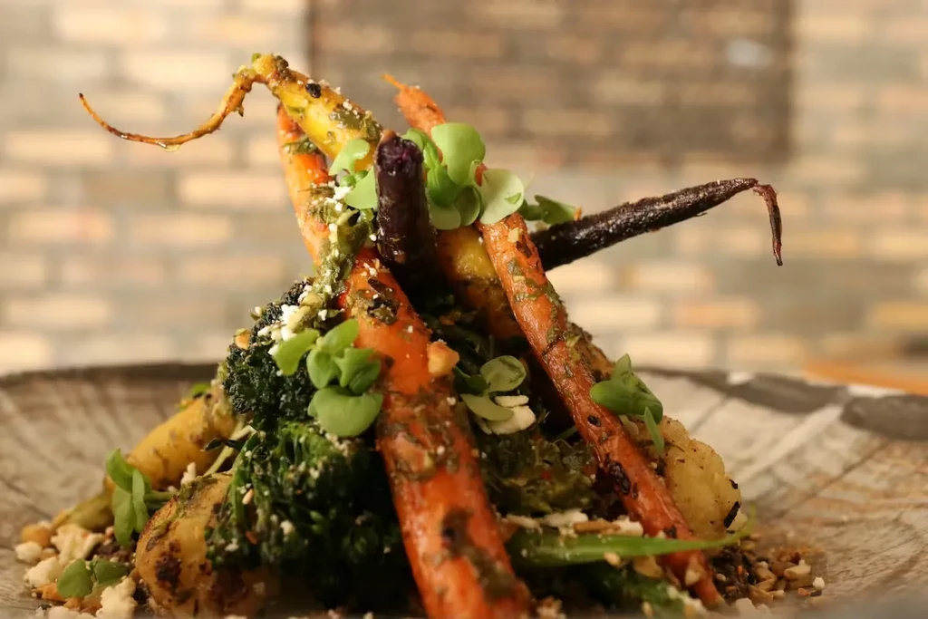 Artfully plated roasted colorful carrots, broccoli, microgreens, cheese, and sauce.