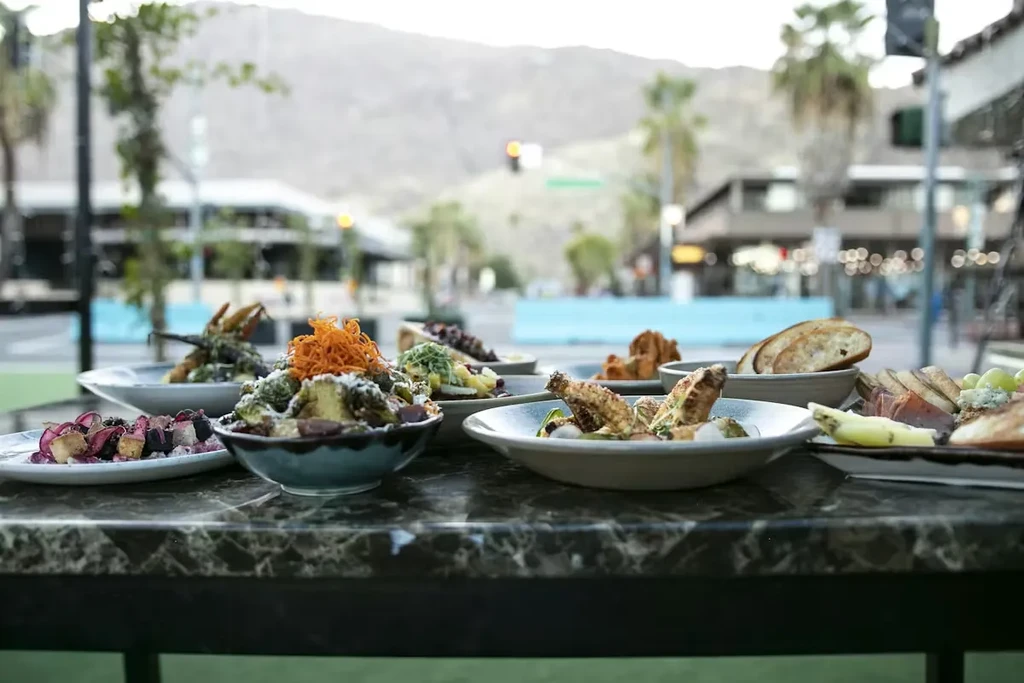 Close-up of roasted vegetables, chicken, bread, and cheese on an outdoor table.