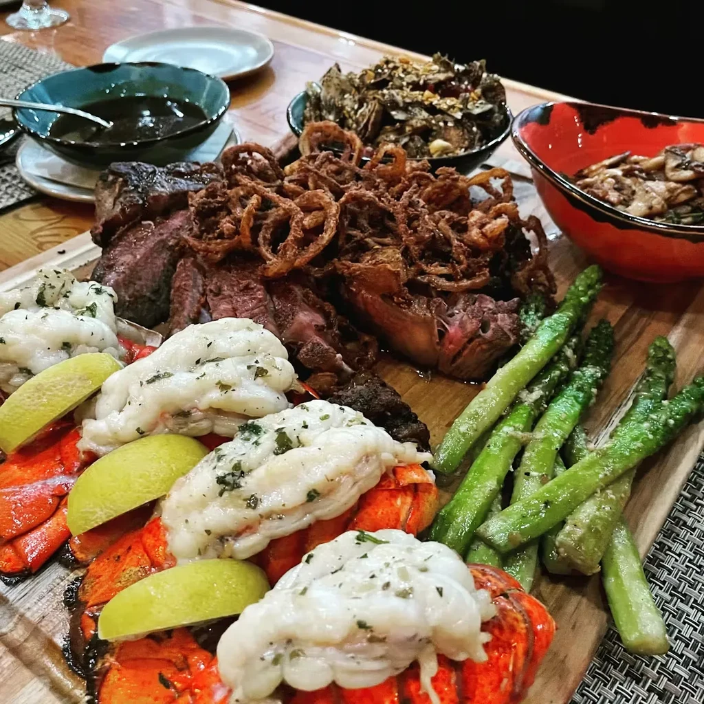 Platter of sliced steak, lobster tails, onion rings, and asparagus.