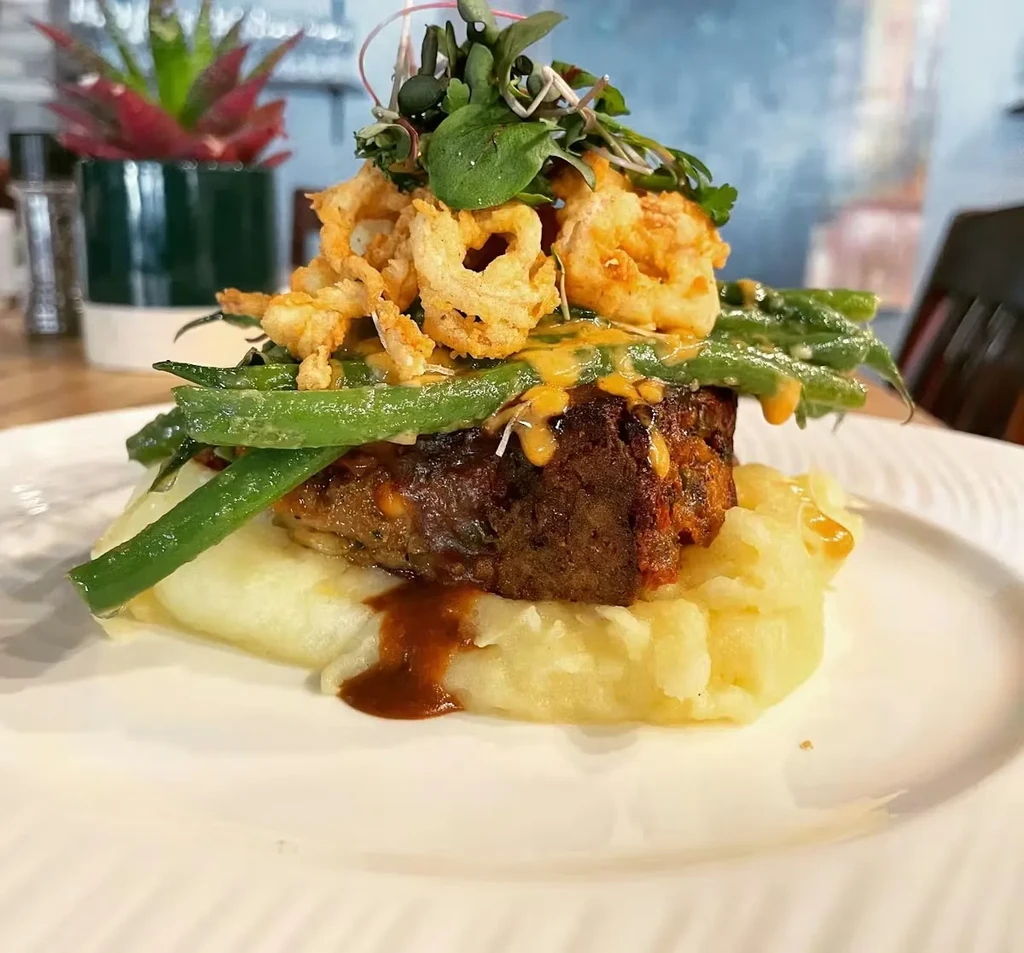 Hearty meat dish on mashed potatoes with green beans and crispy onions.